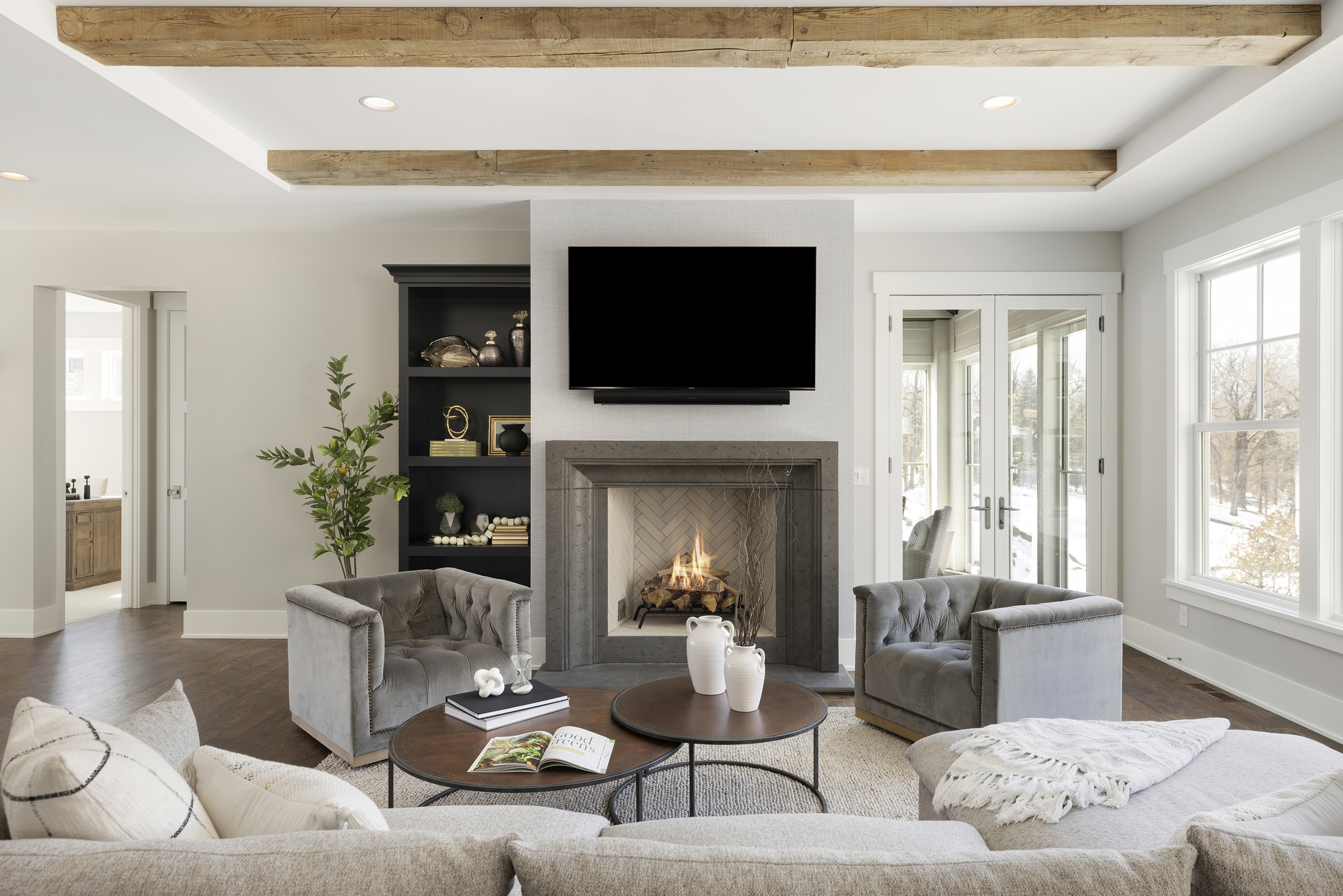 Great room with light grey walls, black built in shelves surrounding a fireplace and a tv with two grey chairs and a grey couch in the living space