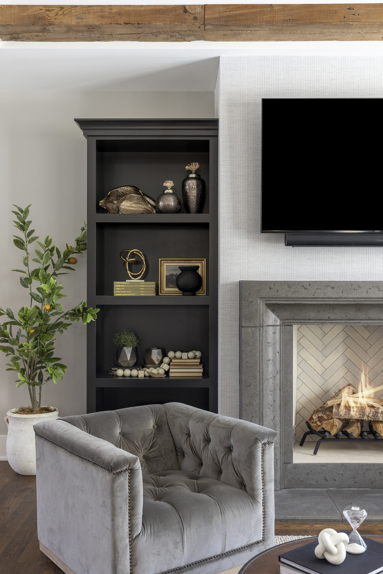 Great room with light grey walls, black built in shelves surrounding a fireplace and a tv with a grey velvet chair