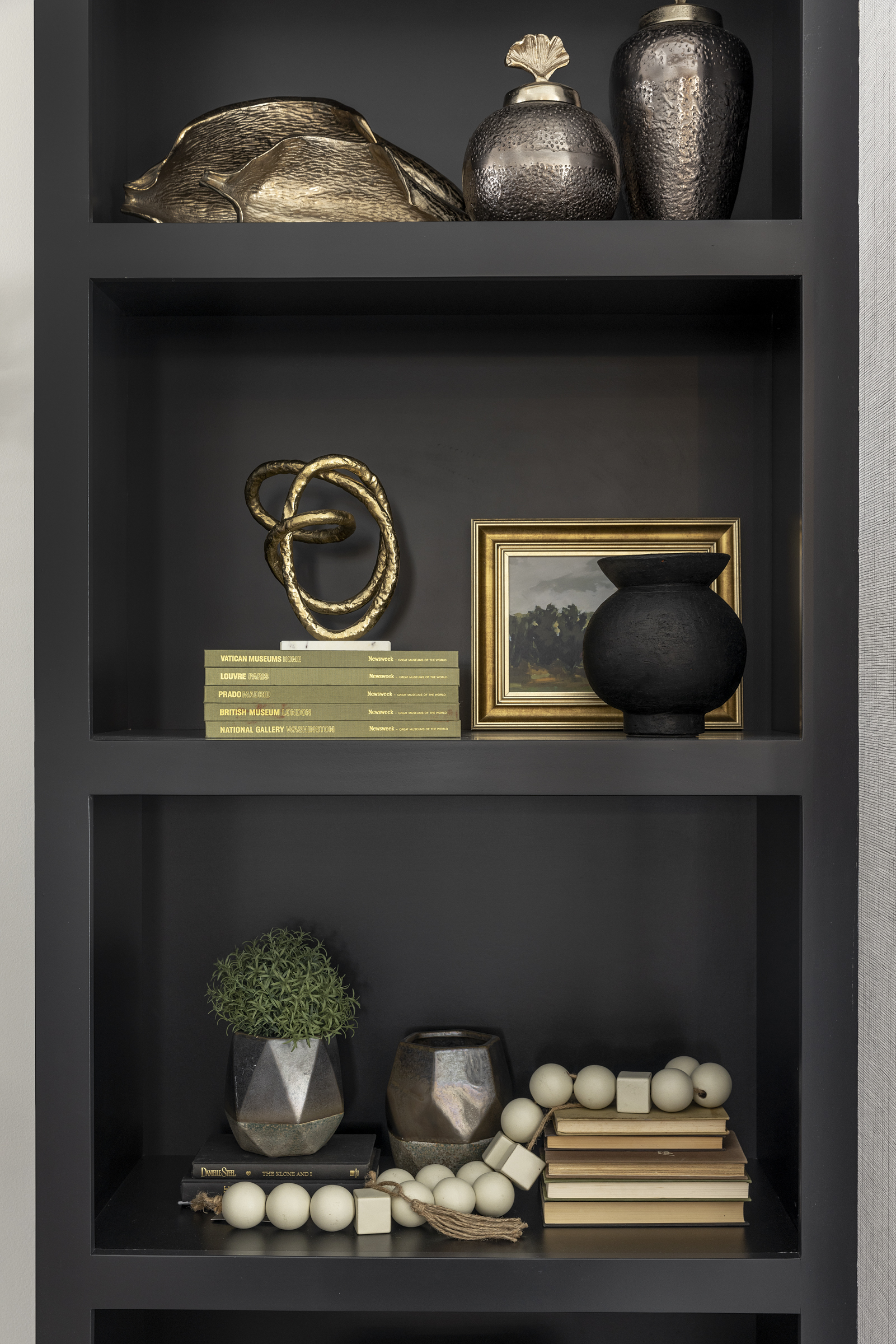 close up look at black built in shelving furnished and decorated with gold accent pieces, picture frames, vases, and books