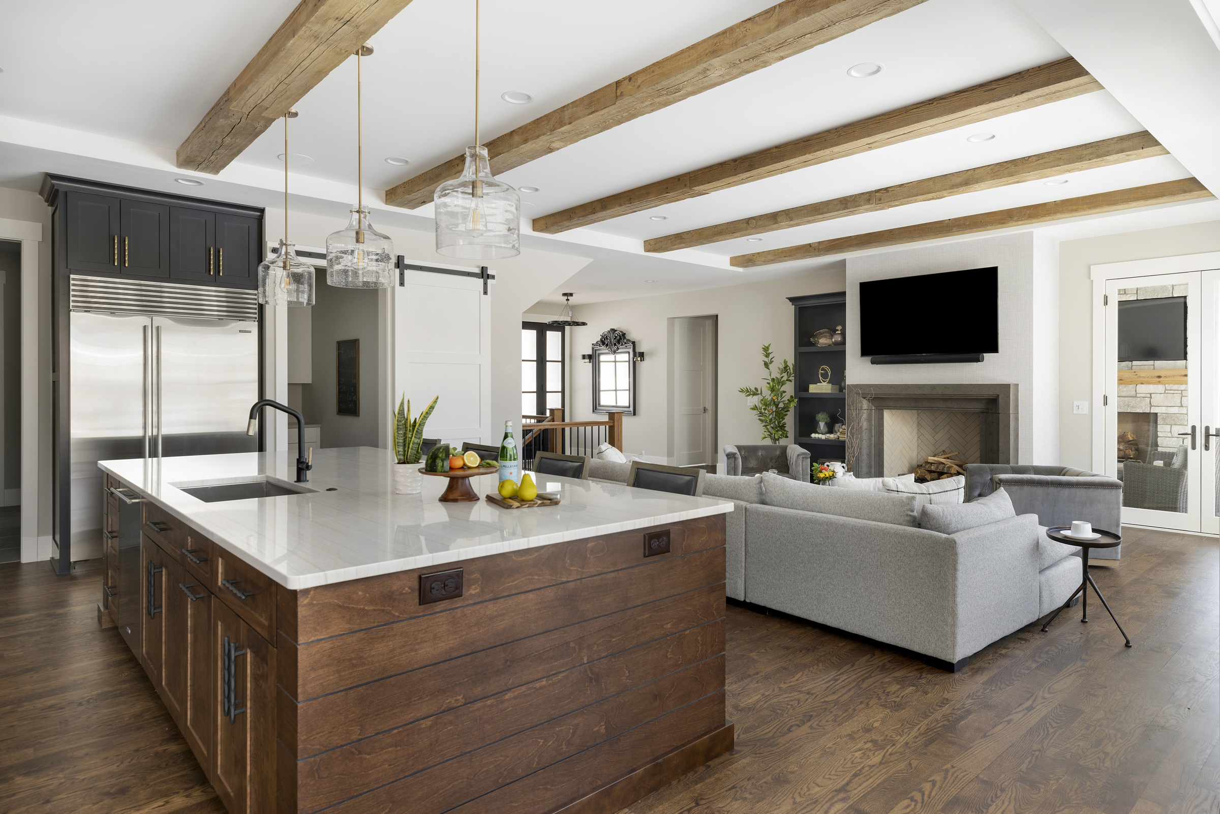 oversized kitchen island with white countertops, wooden ceiling beams, and they grey living room couch in the background