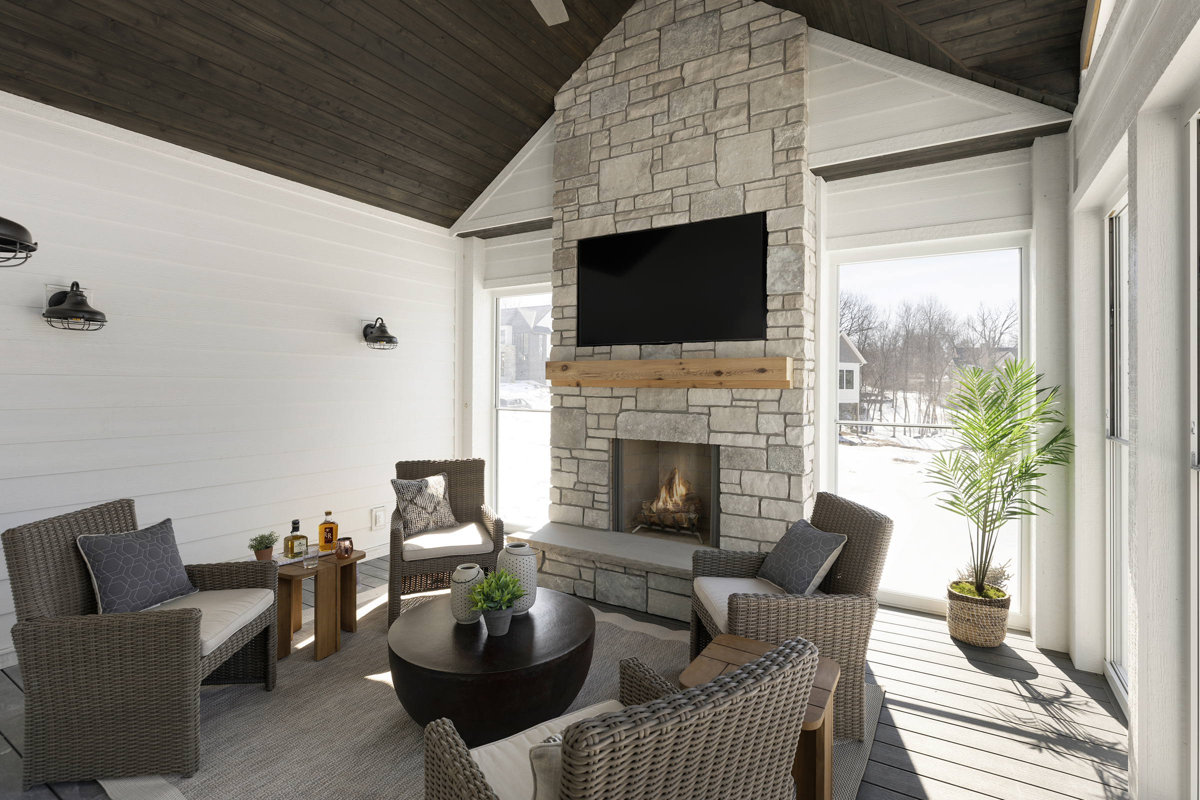 four season porch with arched ceiling detail, stone fireplace surround, floor to ceiling windows, shiplap walls, four patio chairs, and a coffee table