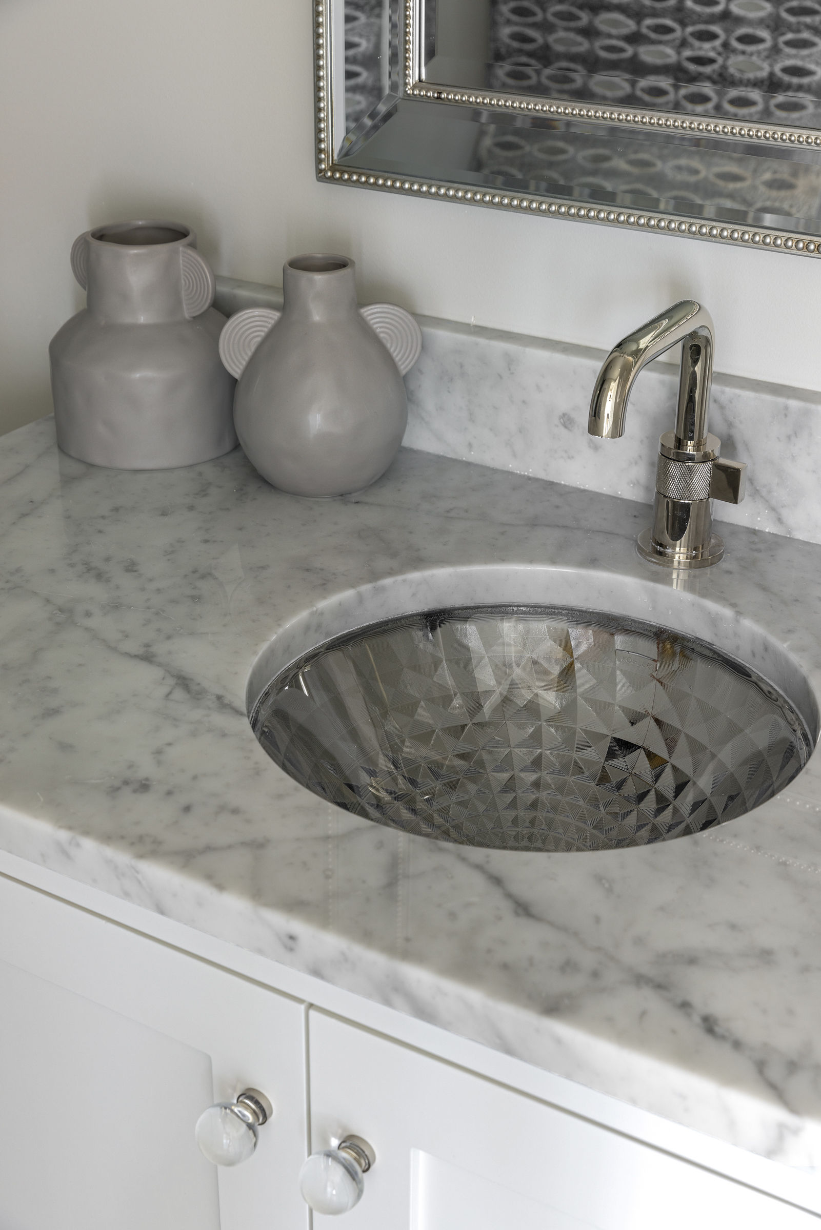 a see through glass sink bowl with a gold faucet, set in to marble counter top, and a white vanity