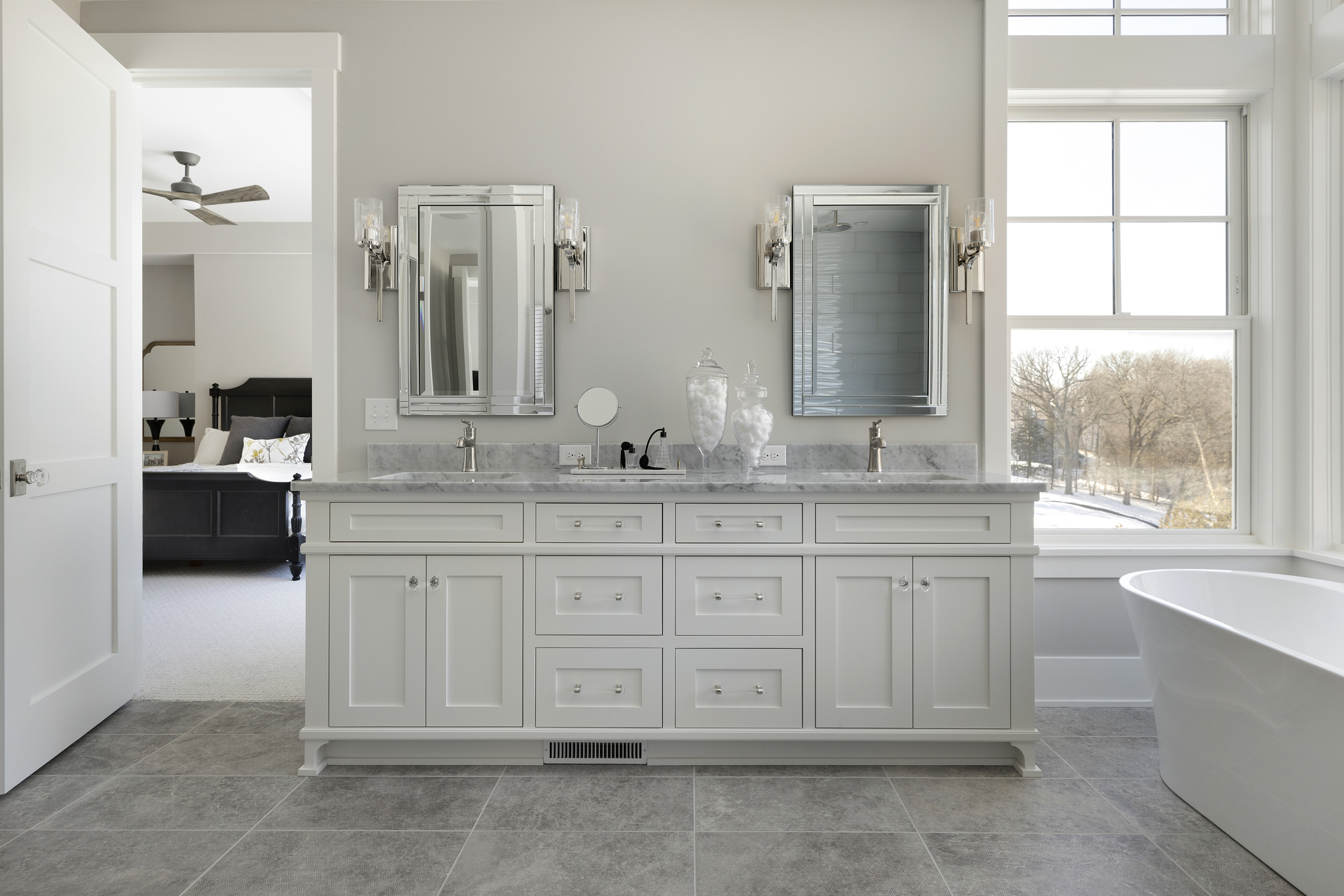 Master bathroom with a double vanity with white cabinets and marbled countertops and a soaker tub on the right