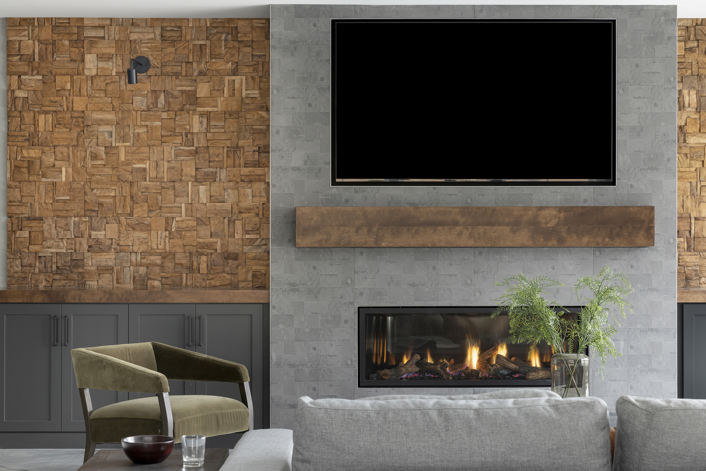 lower level living room with custom hand carved wood accent wall next to a custom stone fireplace surround with a reclaimed wood mantle