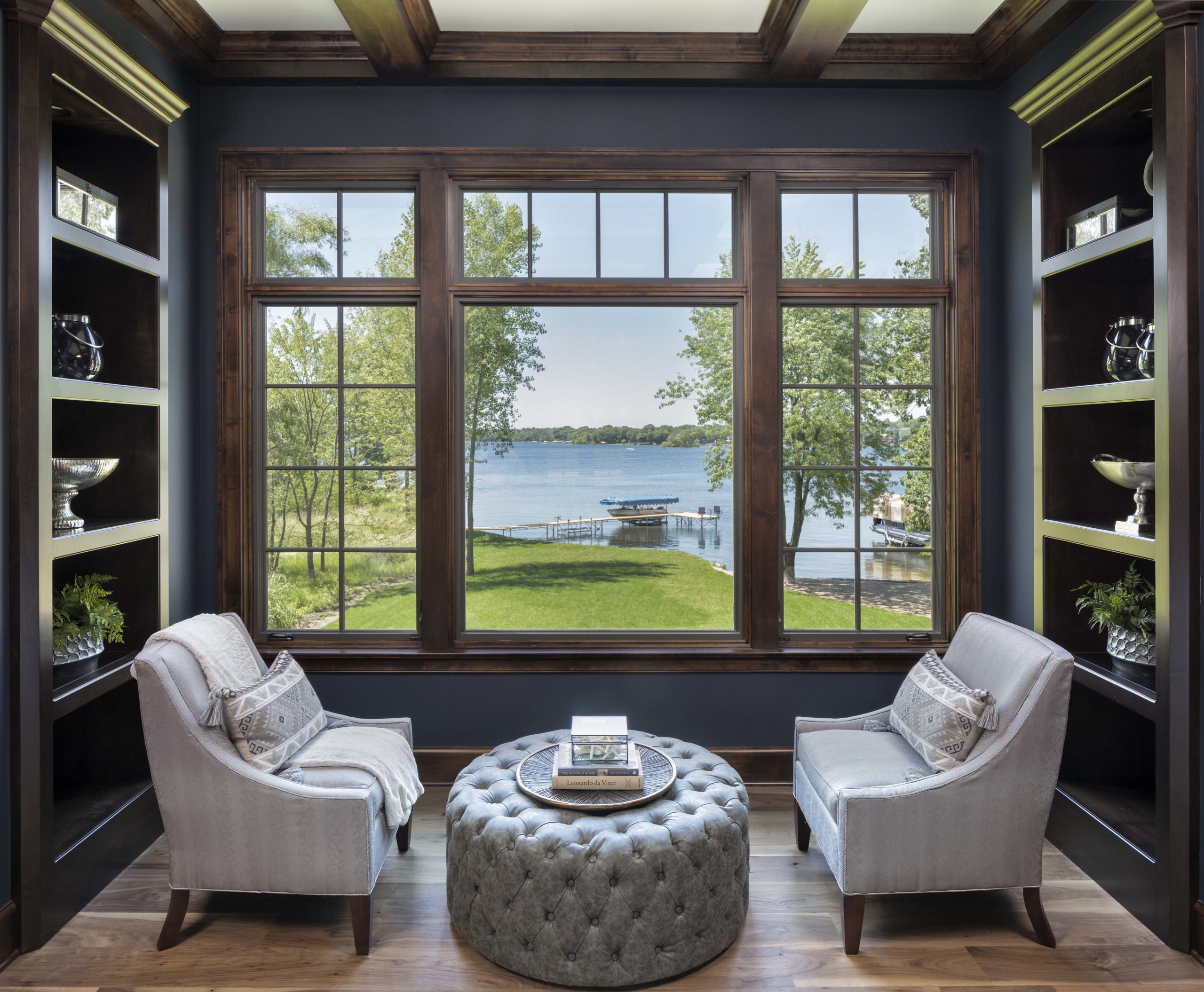 reading nook with two grey chairs and a round ottoman looking out to the lake in the backyard