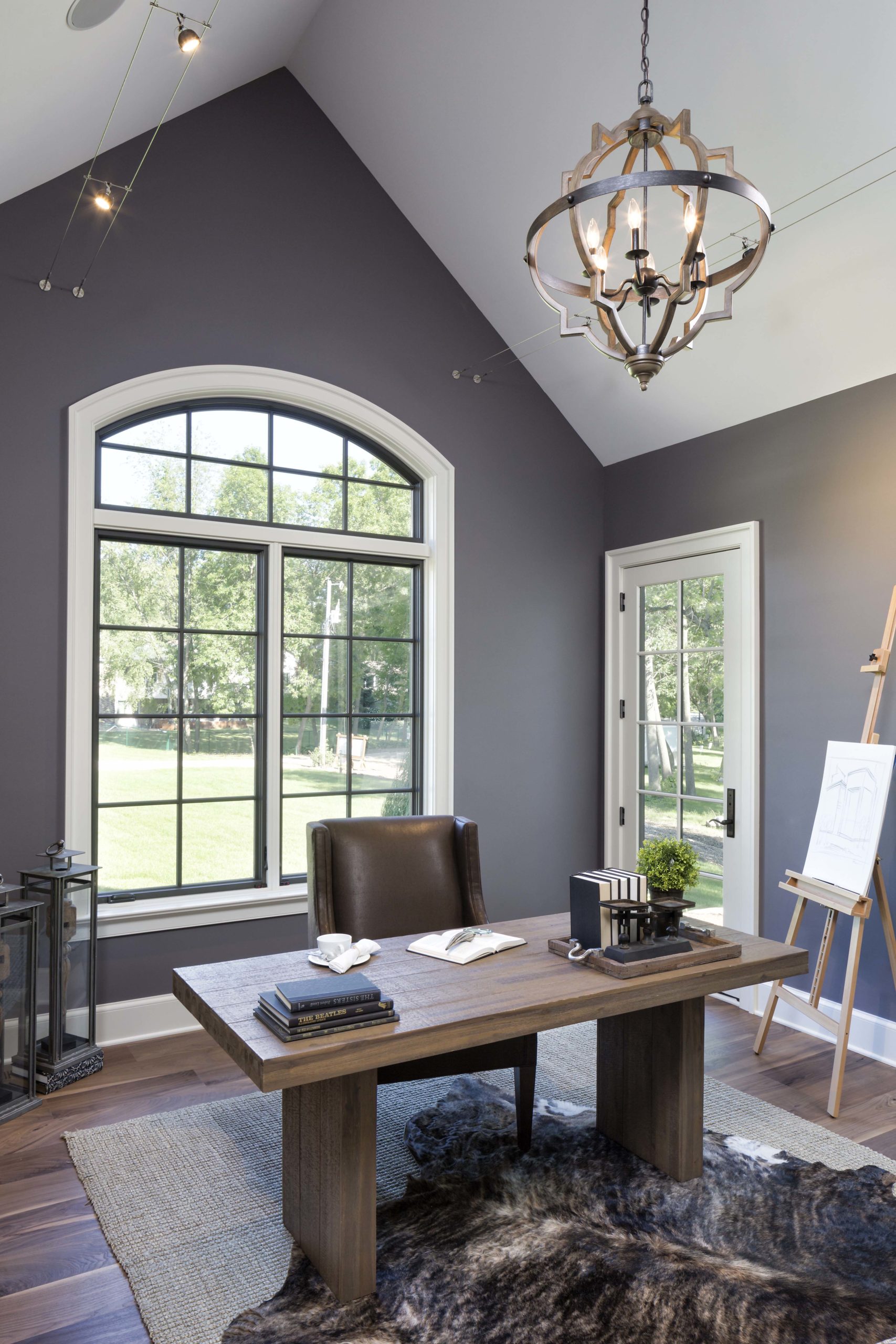 home office with grey walls, a large arched window, and a brown desk in the middle of the room.