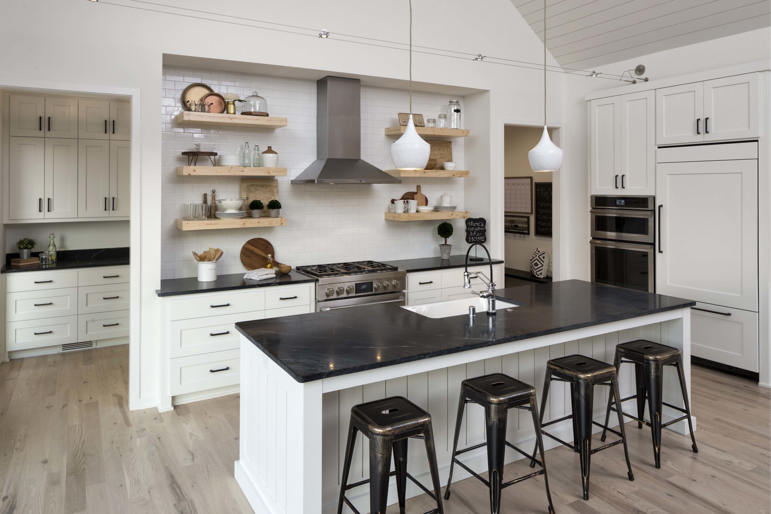White farmhouse kitchen with open shelving, black countertops, and black metal stools