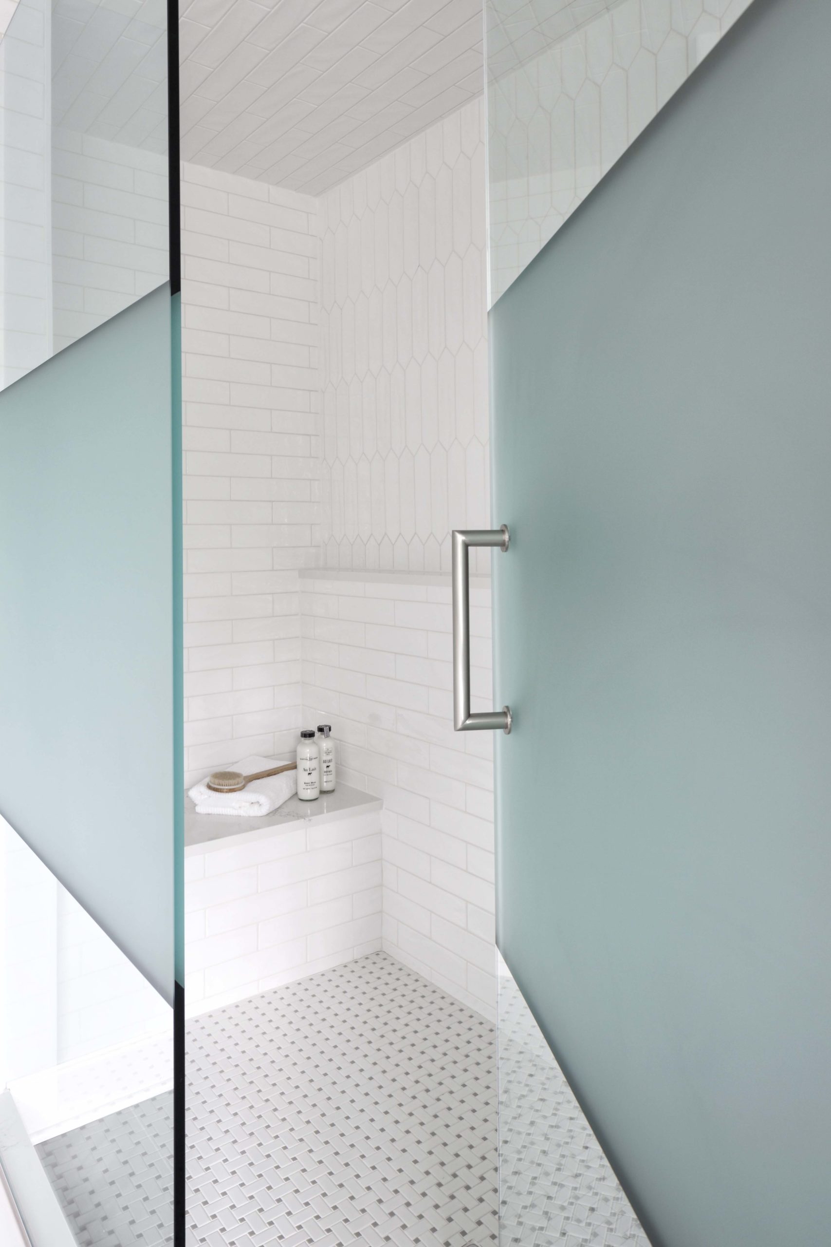 a glass shower door propped open to see the white tile shower inside