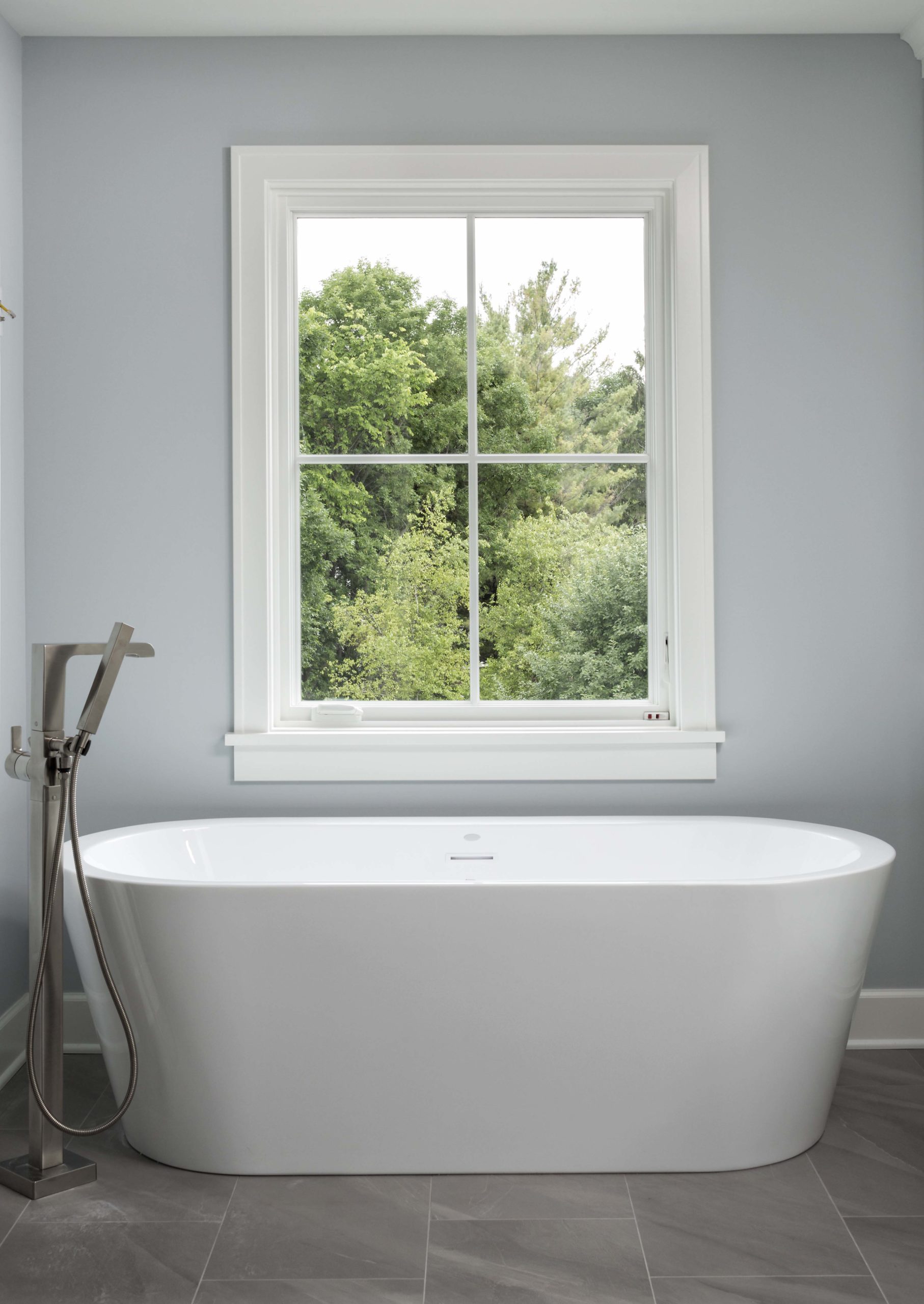 white soaker tub with large window behind it and light blue walls
