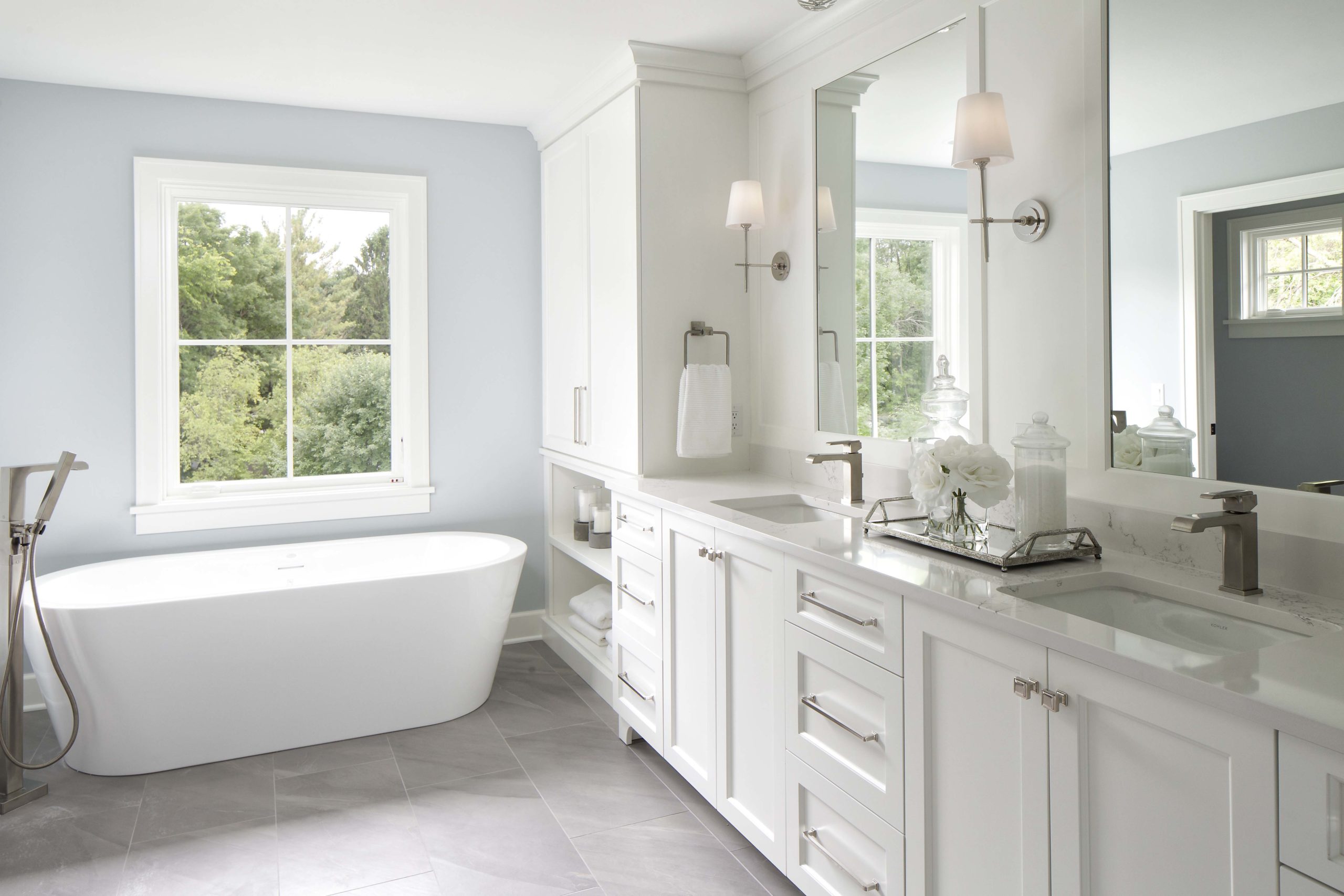 master bathroom with light blue walls, a white soaker tub, and dual white vanities