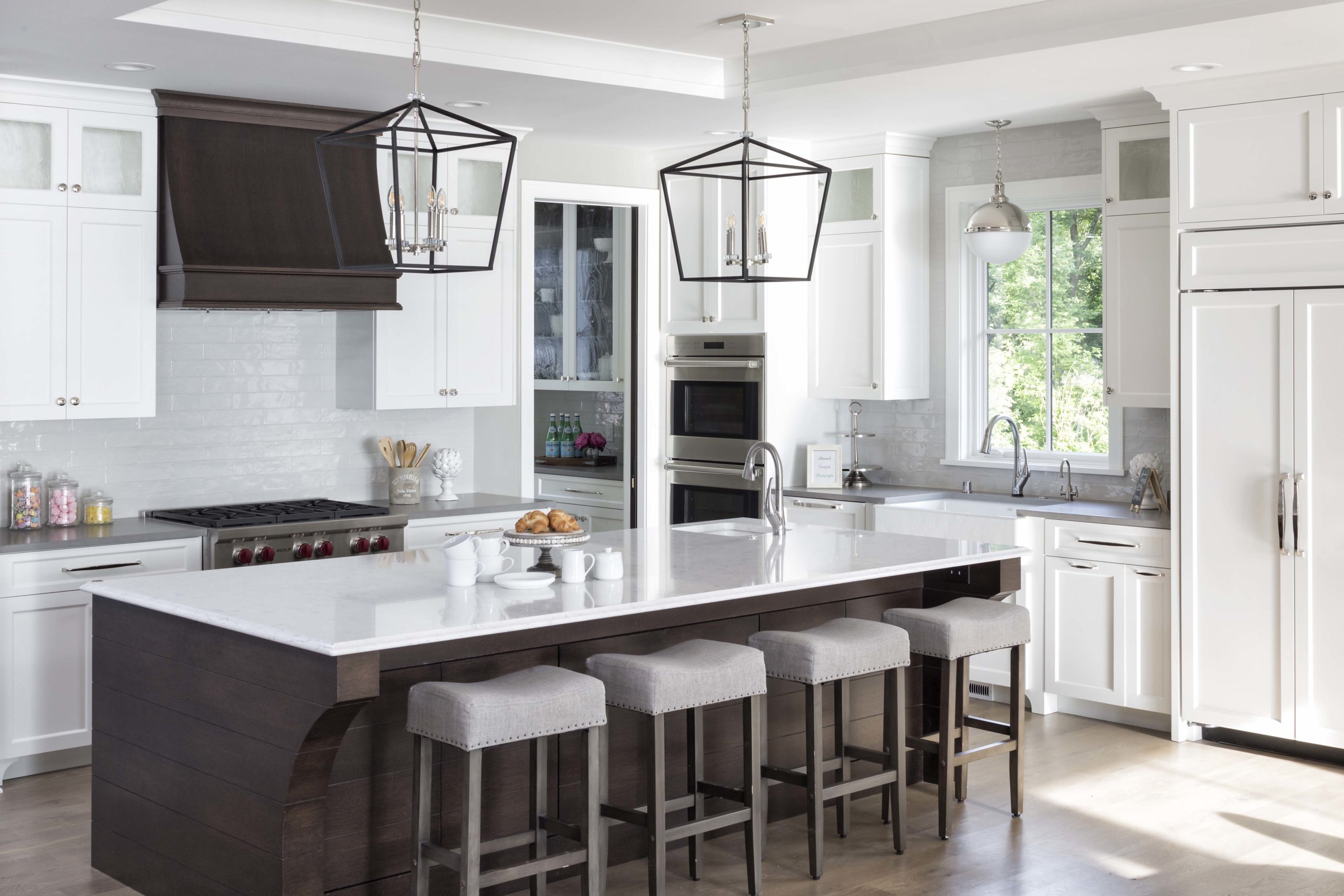 white kitchen with white countertops, dark brown island, and four stools at the island