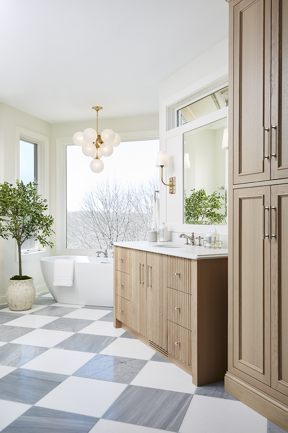 Master bathroom with checkered tile floors, a white standing soaker tub, a chandelier over the tub, and an oak wood vanity