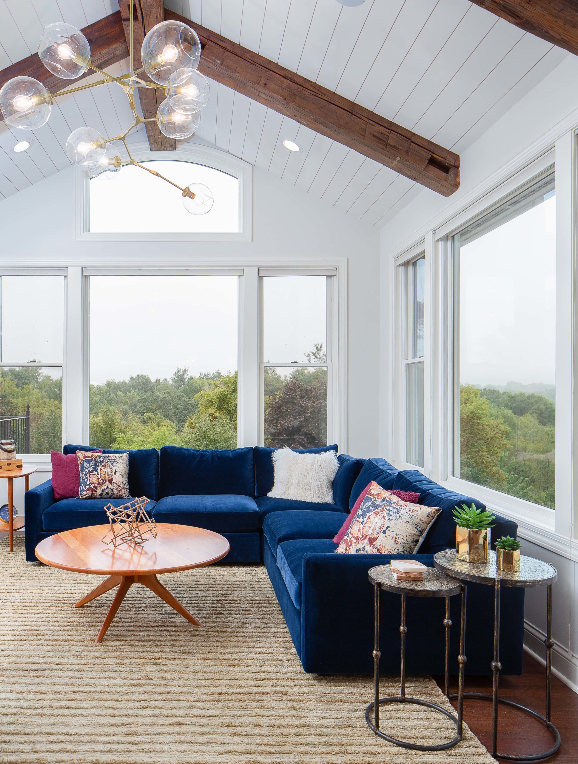 white shiplap porch furnished with a blue velvet couch, pink patterned pillows, and reclaimed wood ceiling beams