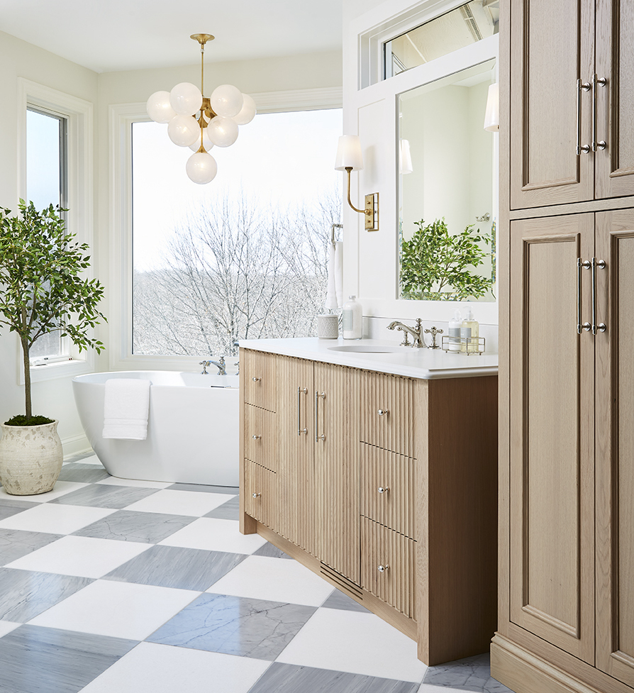 remodeled master bathroom with checkered pattern tile floors and natural wood cabinetry and a soaker tub in the background