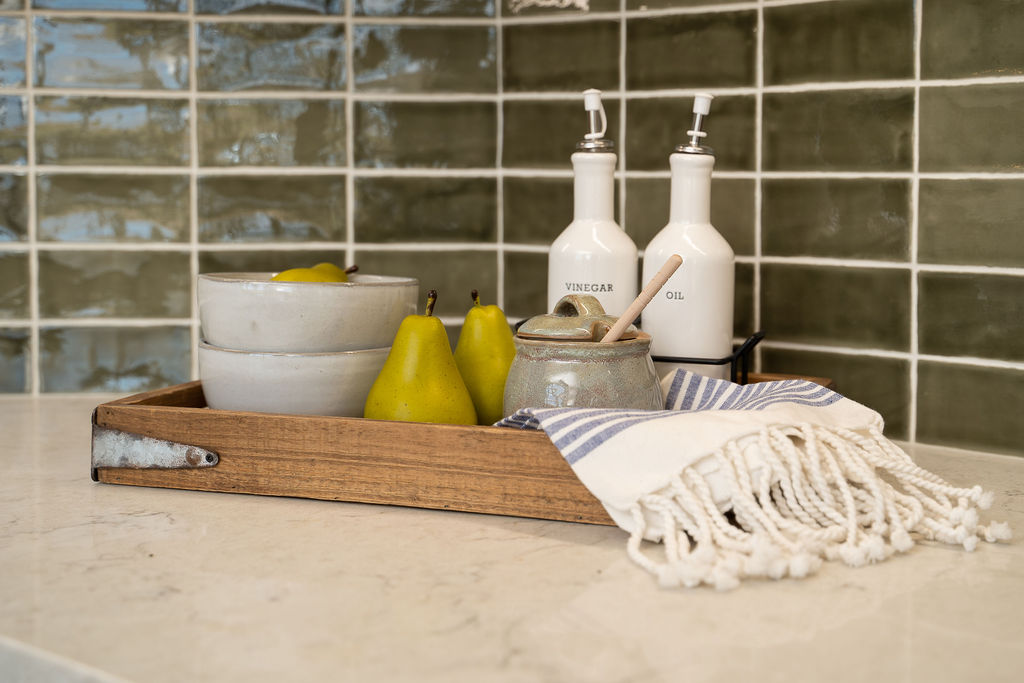 Kitchen decor sitting in a wooden tray on the counter with a green tile backsplash in the background