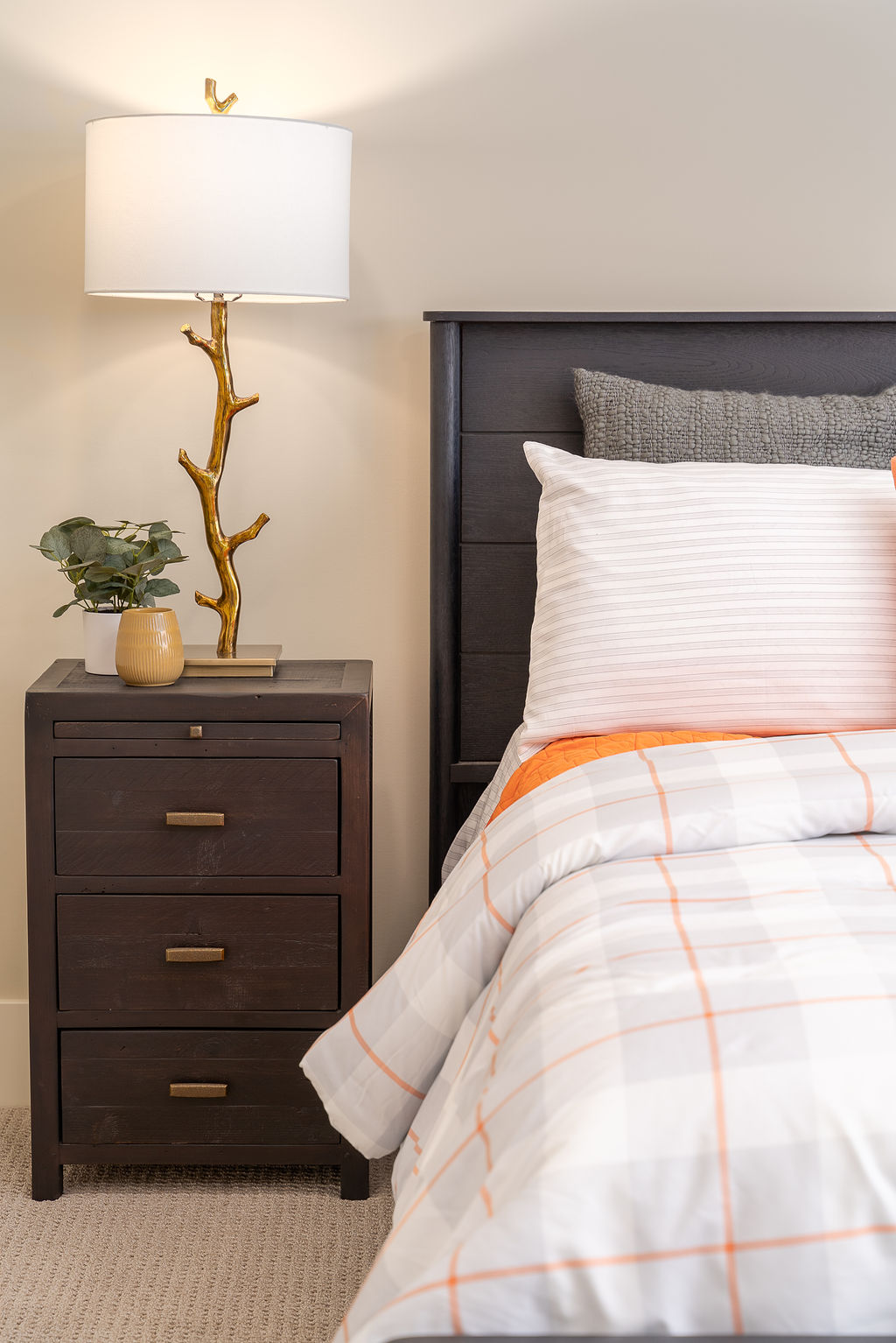 bed with black headboard and night stand, orange and white bedding, and a white lamp