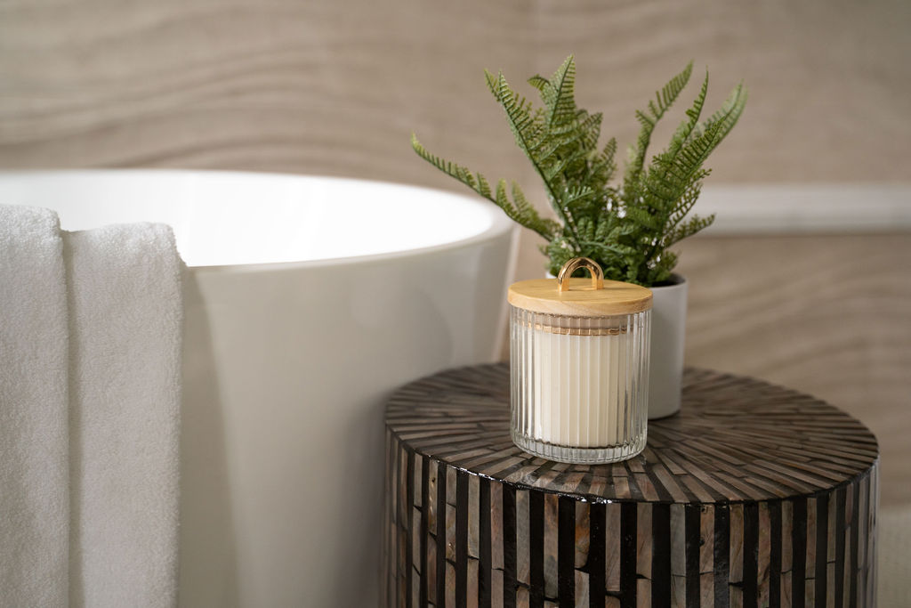 a candle and a plant sitting on a side table next to a white bathtub