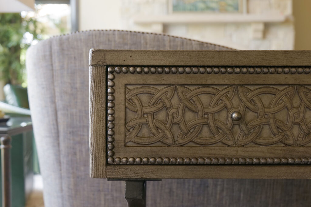 A modern side table in a living room with ornate carvings.