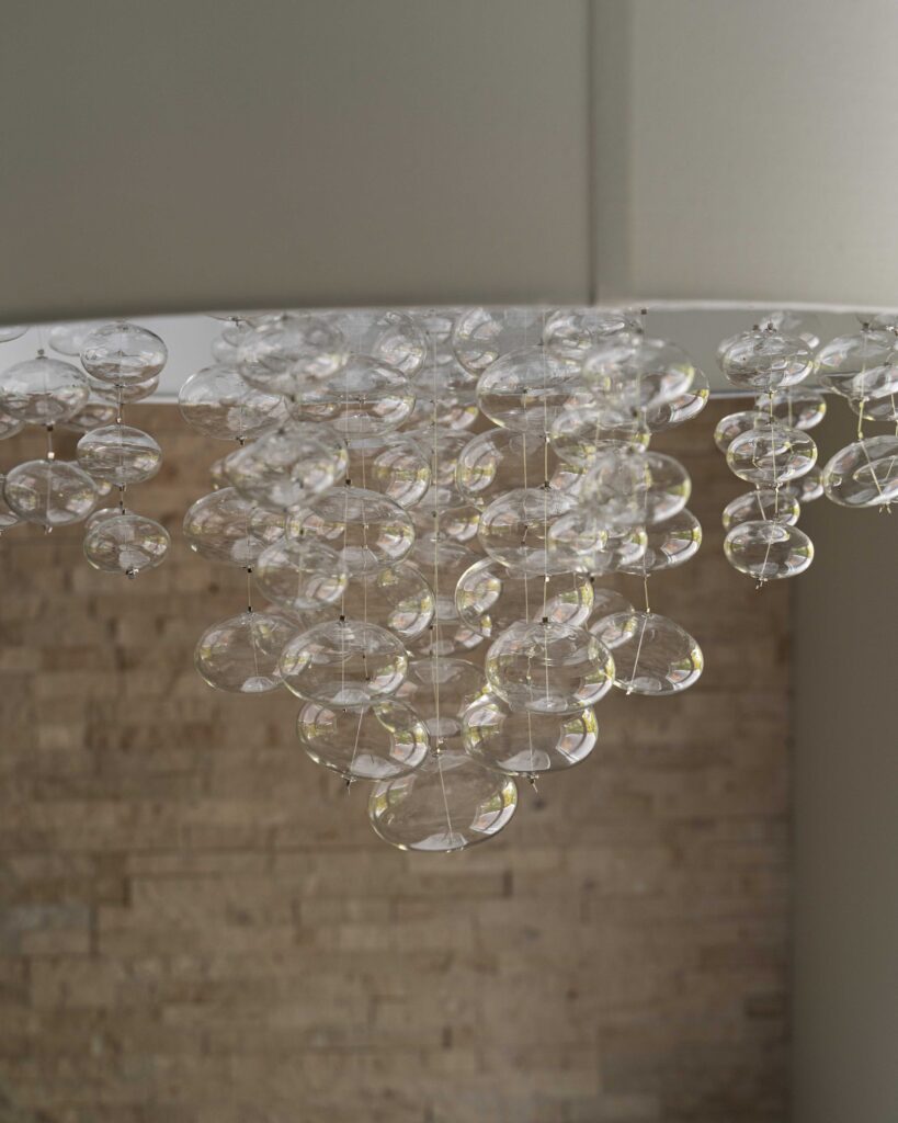 A chandelier made of glass bubbles hanging from a brick wall in a woodside road remodel.