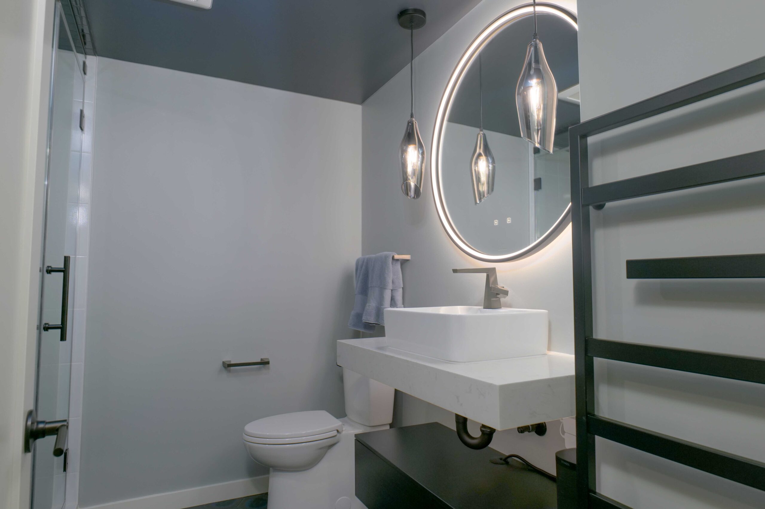 A modern bathroom with a round mirror above the sink in an Orchard Lake remodel.