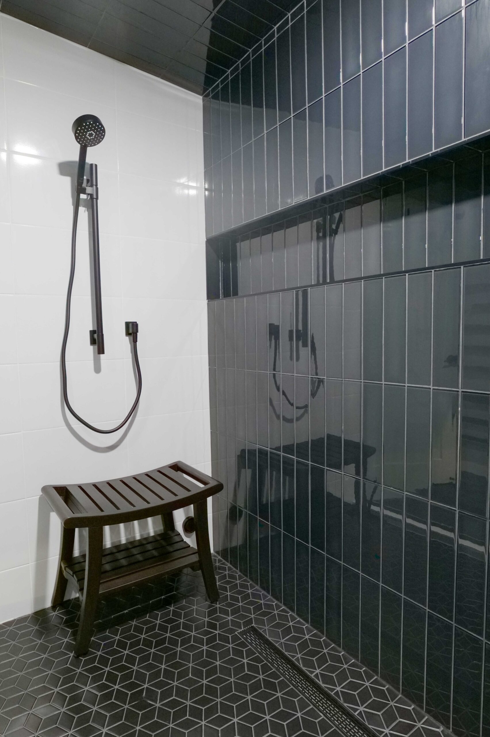 Orchard Lake remodel: A black and white tiled shower with a wooden bench.