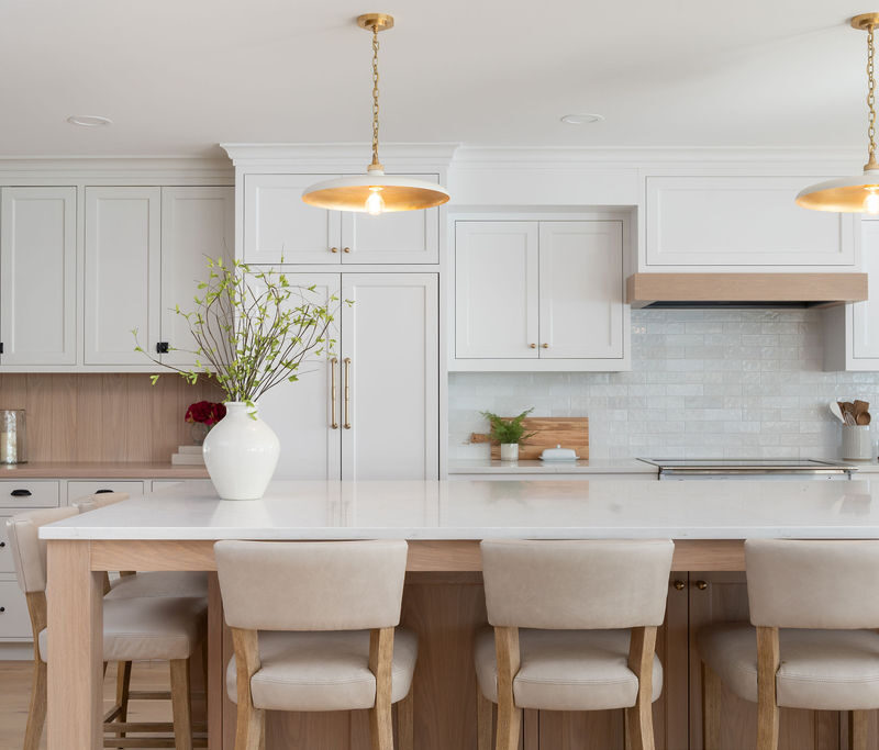 Modern kitchen on Shoreline Boulevard featuring white cabinets, a large island with beige stools, pendant lights, and a stylish vase of branches.